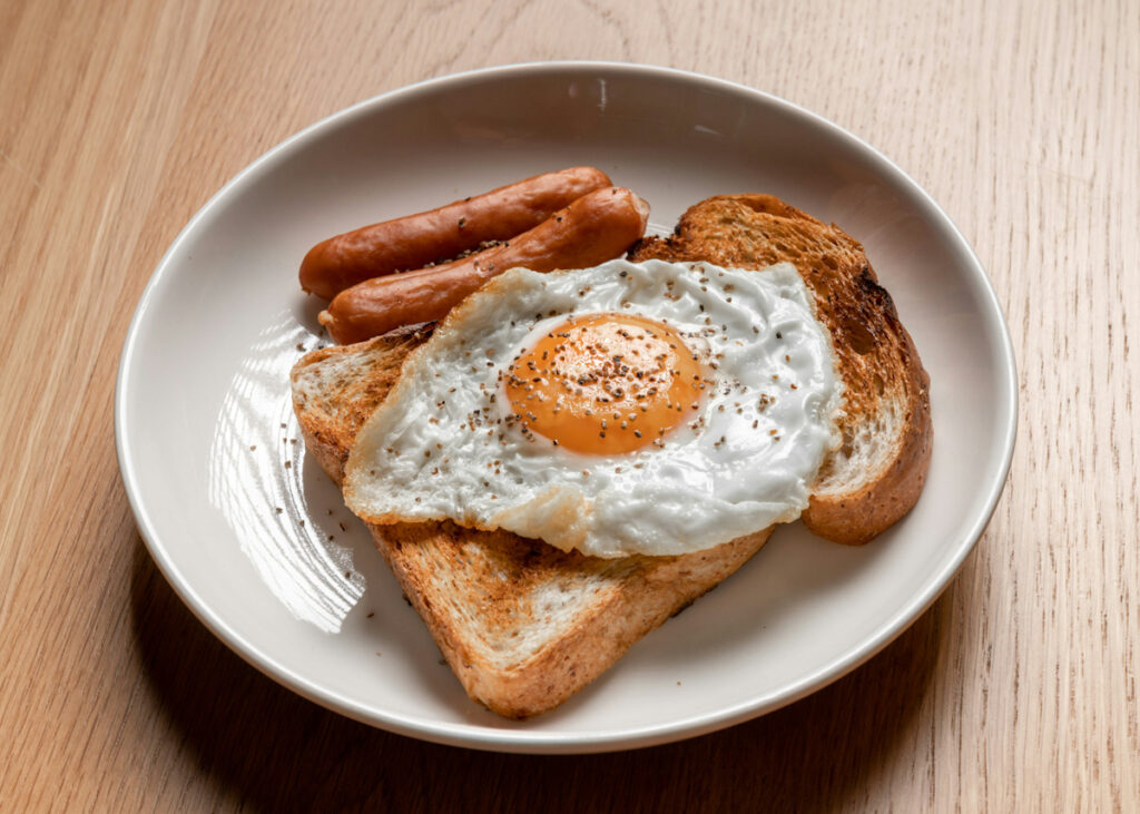 A breakfast plate with a piece of toast, a hard fried egg, and 2 sausage links