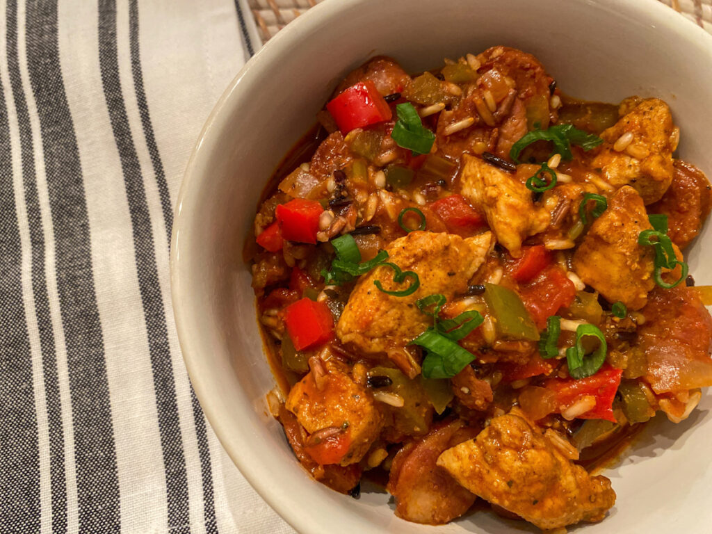 Healthier chicken jambalaya in a bowl with chunks of chicken, sausage, red and green peppers, green onion, and rice