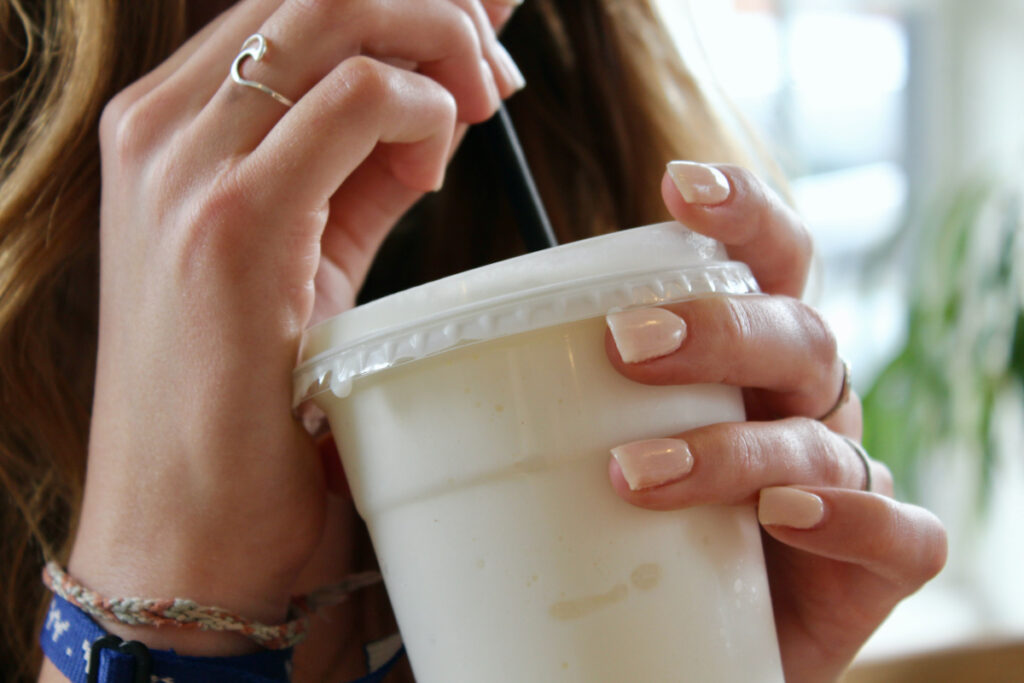 Woman drinking a protein shake from a plastic to go cup.
