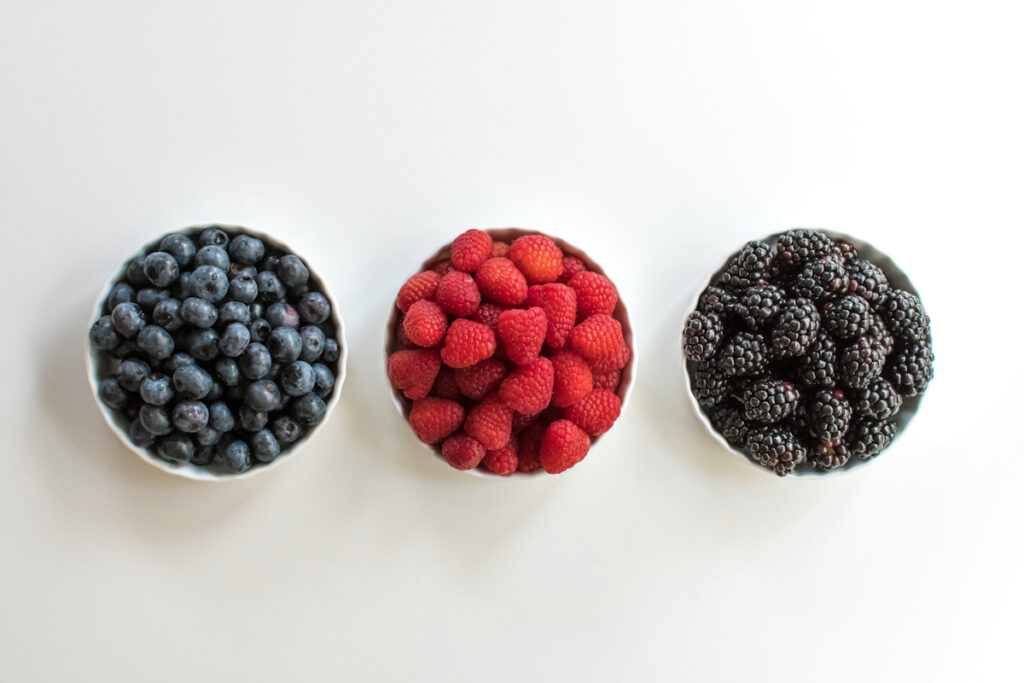 A bowl of blueberries, a bowl of raspberries, and a bowl of blackberries.