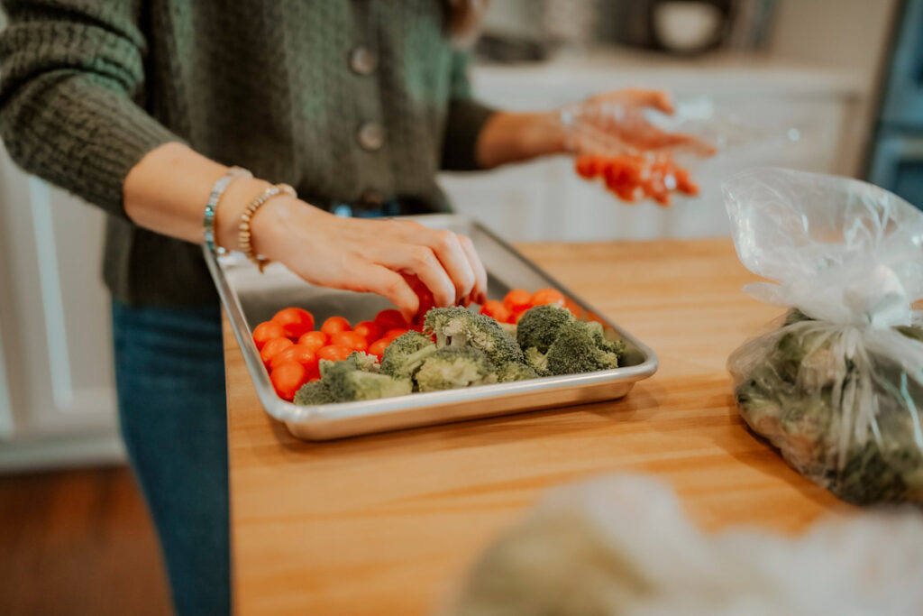 Woman putting cherry tomatoes on a baking sheet with broccoli florets.