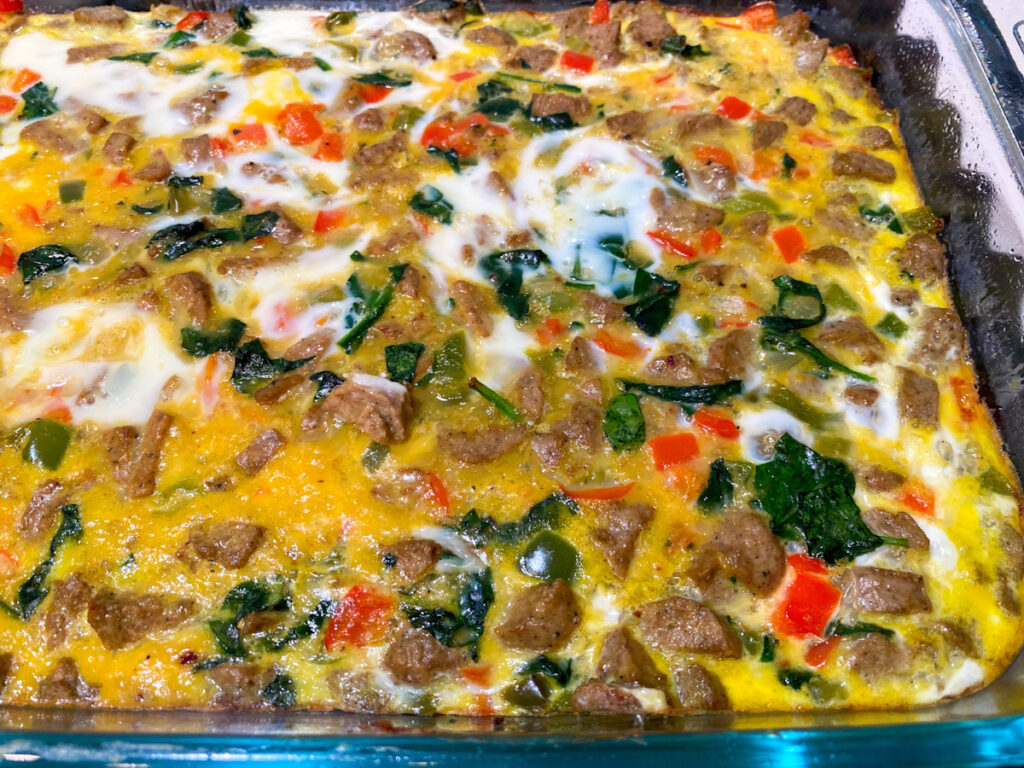 A baked breakfast casserole in a glass dish with cooked egg, turkey sausage, peppers, and spinach.