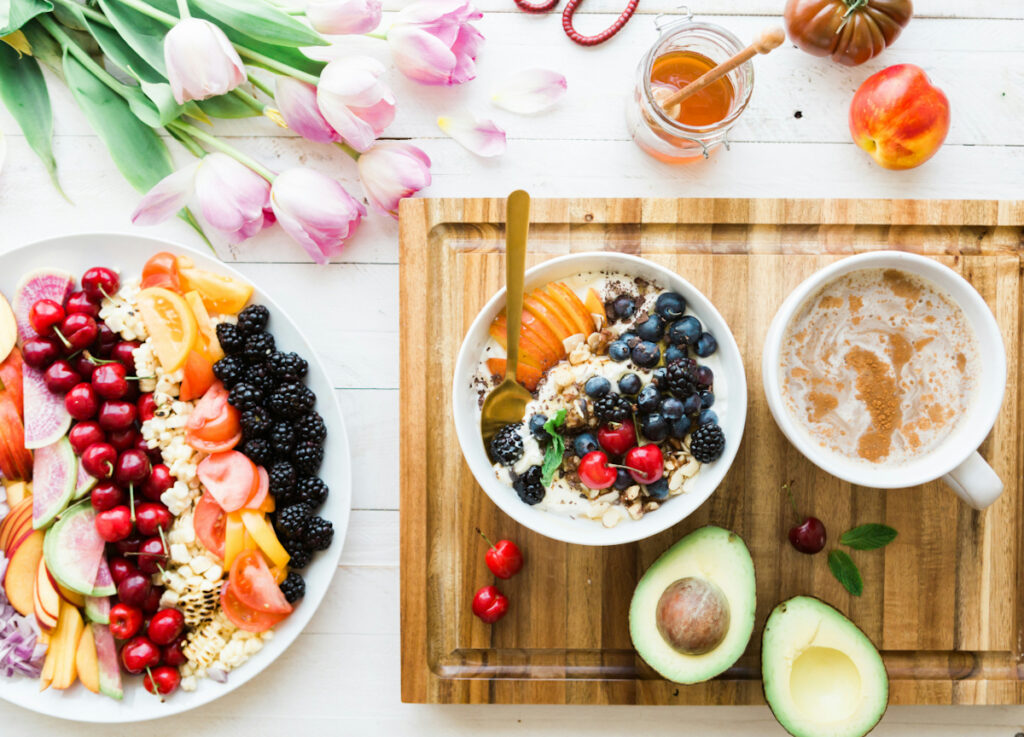 A large plate of berries and produce, a small bowl of a yogurt parfait with apples, cherries, and blueberries, and a cup of coffee.
