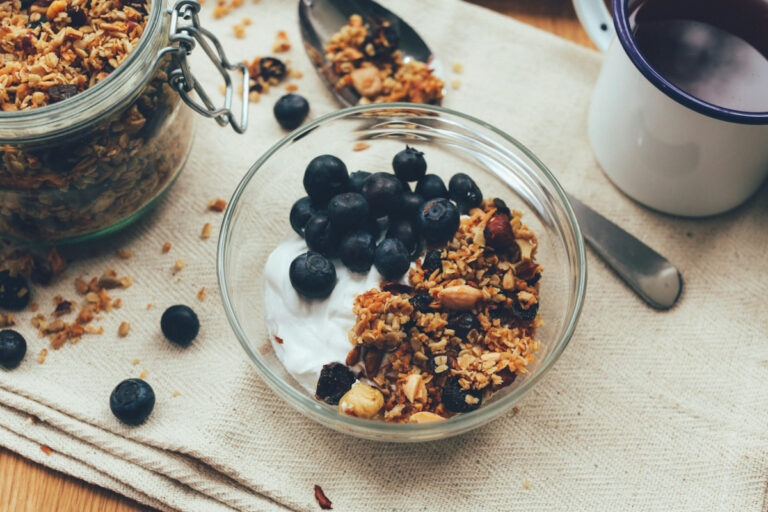 Bowl of yogurt with blueberries and granola with a spoon and jar of granola