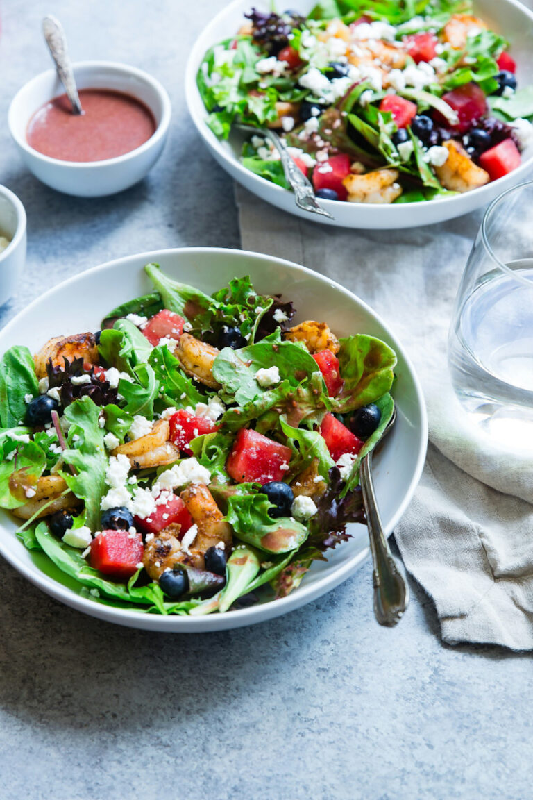 Two bowls of salads with spinach, strawberries, blueberries, nuts, feta cheese, and a small dish of raspberry vinaigrette dressing.