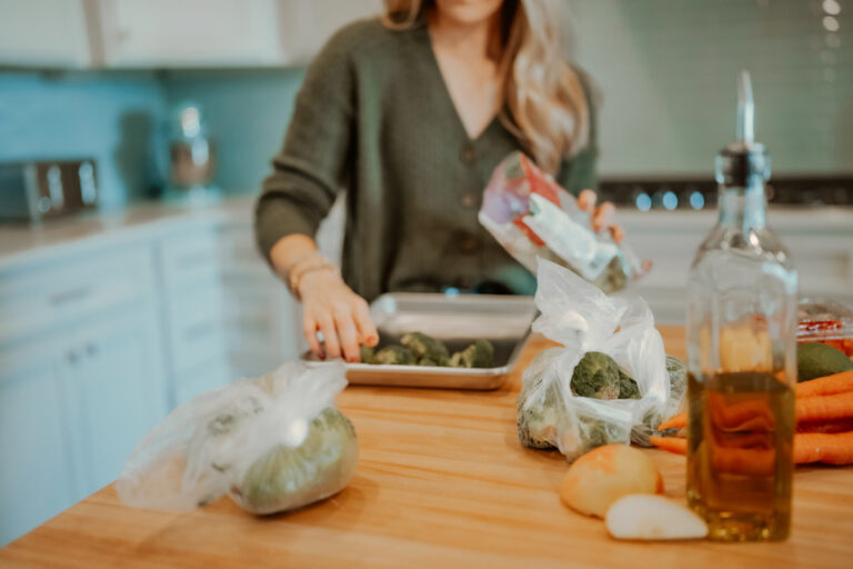 Woman loading broccoli florets onto a baking sheet and meal prepping in the kitchen.