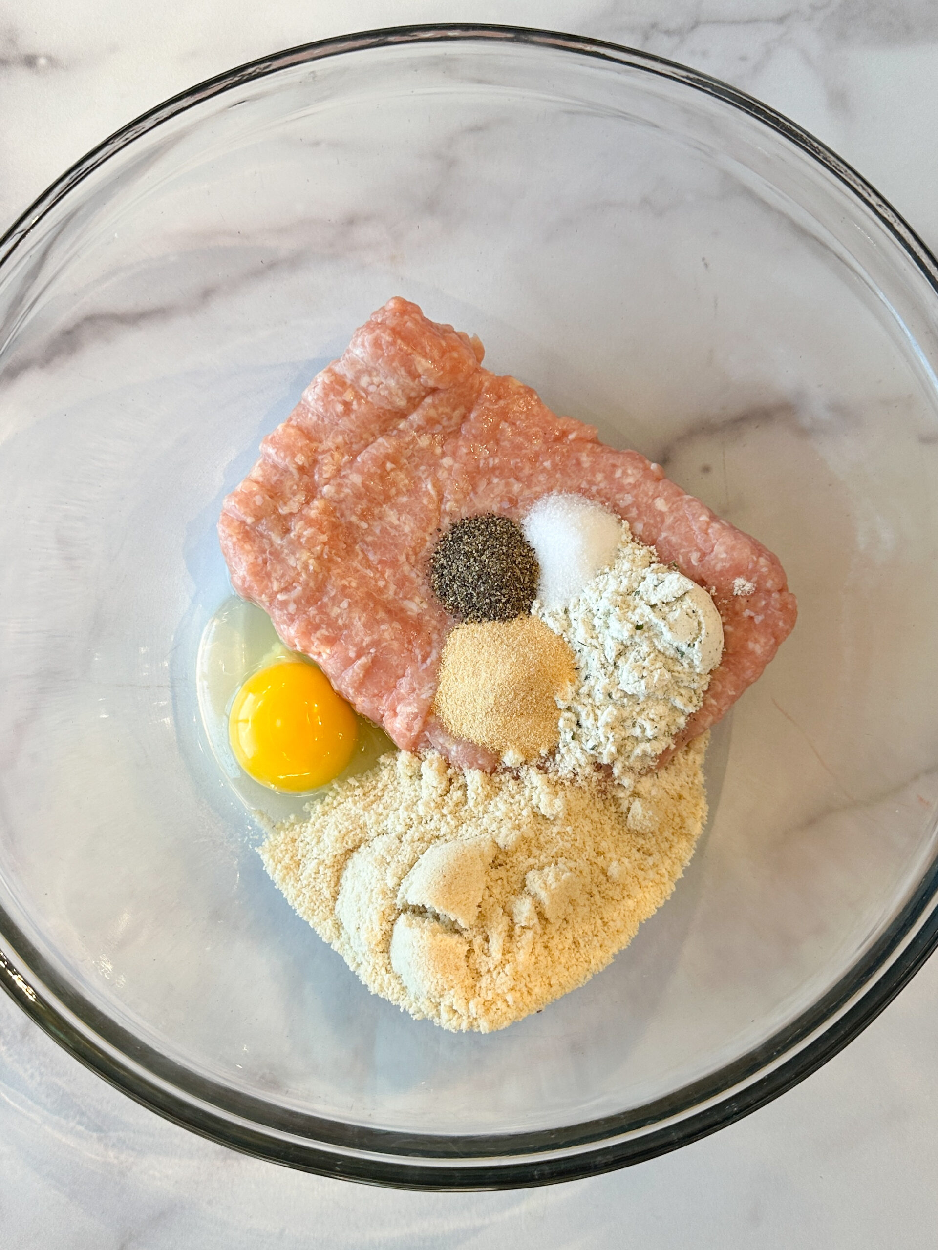 healthy buffalo chicken meatball ingredients poured into a mixing bowl: ground chicken, egg, seasonings, almond flour, and ranch mix.