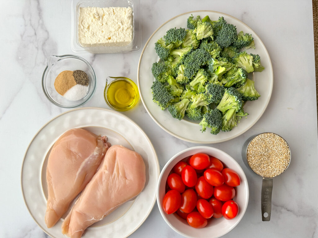 Chicken breast, chopped broccoli florets, cherry tomatoes, quinoa, seasonings, olive oil, and a block of feta cheese