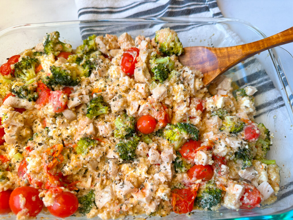 Chicken Quinoa & Feta Bake in a casserole dish with cubed chicken, broccoli, tomatoes, creamy feta, and basil sprinkled on top.