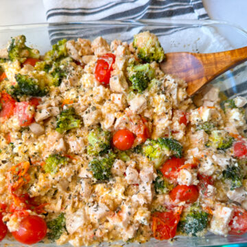 Chicken Quinoa & Feta Bake in a casserole dish with cubed chicken, broccoli, tomatoes, creamy feta, and basil sprinkled on top.
