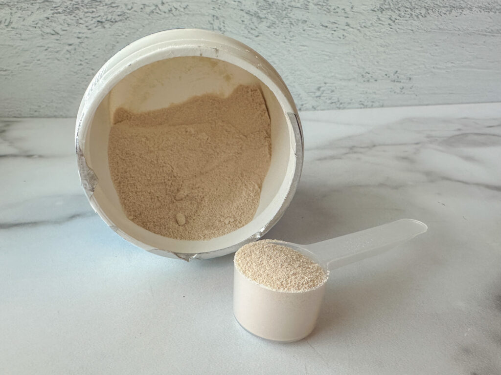Powdered colostrum supplement in a scoop with the supplement in the background