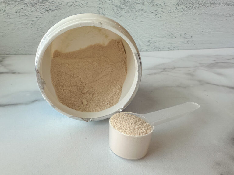 Powdered colostrum supplement in a scoop with the supplement in the background