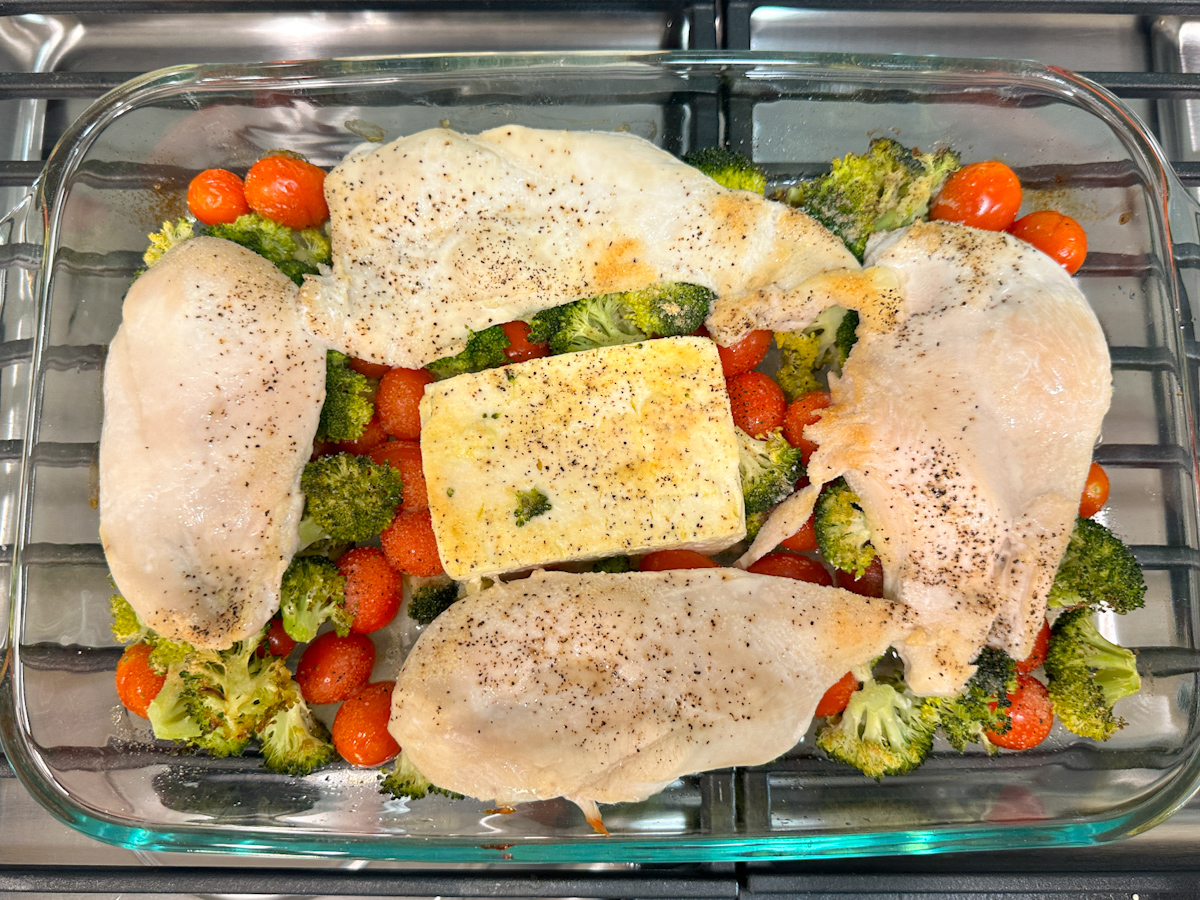 tomatoes and broccoli with feta in the middle and 4 thin chicken breasts on top in a casserole dish.