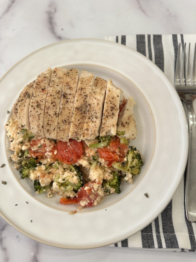 white plate with broccoli, tomatoes, and feta chunks with grilled sliced chicken on top. 