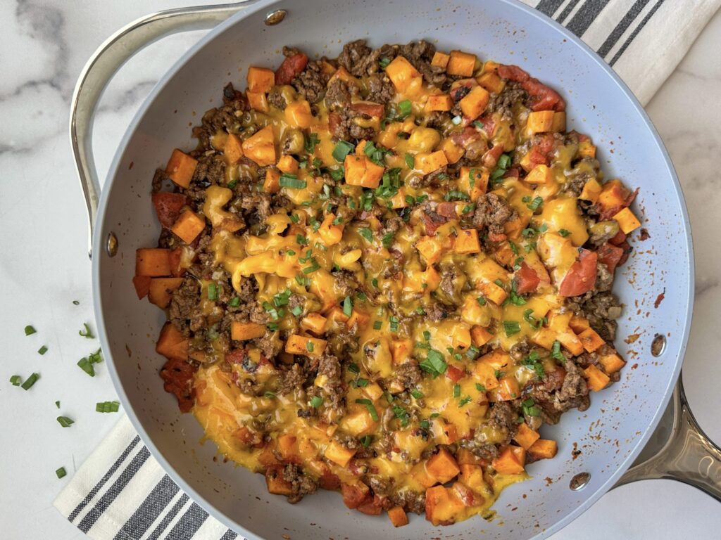 A pan with all ingredients mixed in: sweet potatoes, tomatoes, ground beef, cheese, chopped green onions. It's colorful and looks so warm and cozy.