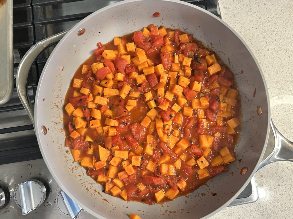 A skillet with cubed sweet potatoes and fire roasted tomatoes being sauteed.