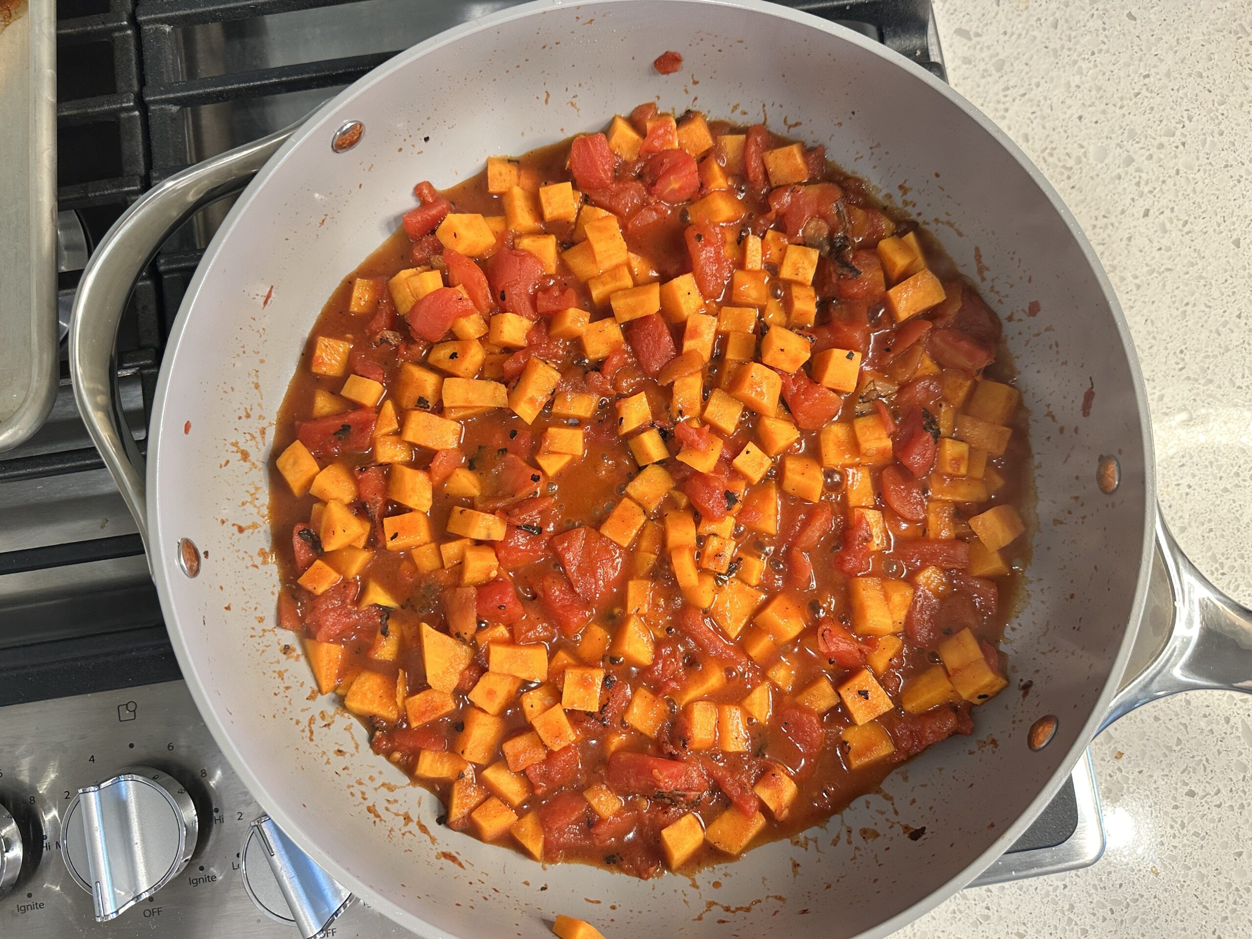 sweet potatoes and tomatoes sauteeing in spices and diced onions in a large skillet.