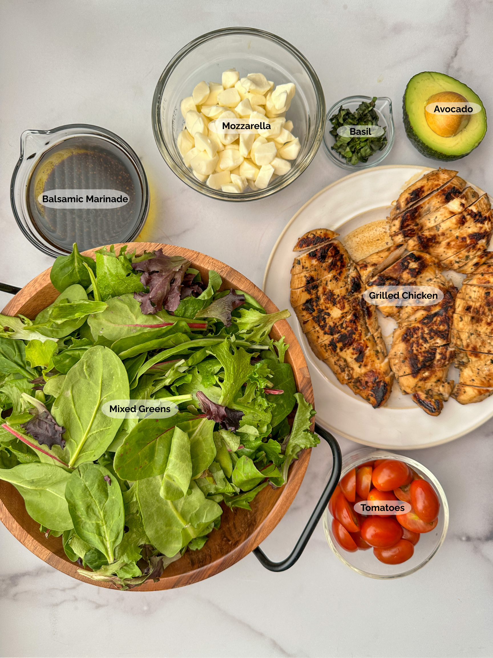 Balsamic Chicken Caprese Salad ingredients: balsamic marinade, mixed greens, fresh mozzarella balls, chopped basil, avocado half, grilled sliced chicken breasts, sliced tomatoes.