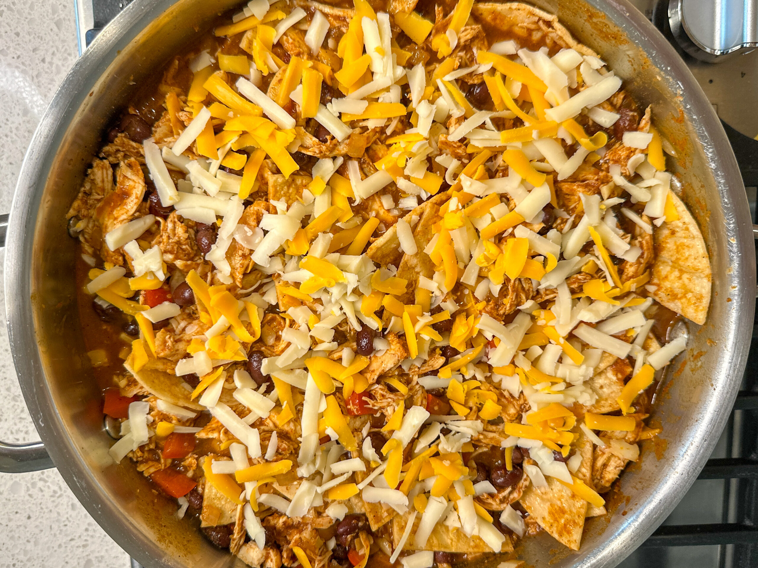 enchilada skillet ingredients in a large skillet: tortilla pieces, shredded chicken, black beans, red bell peppers.