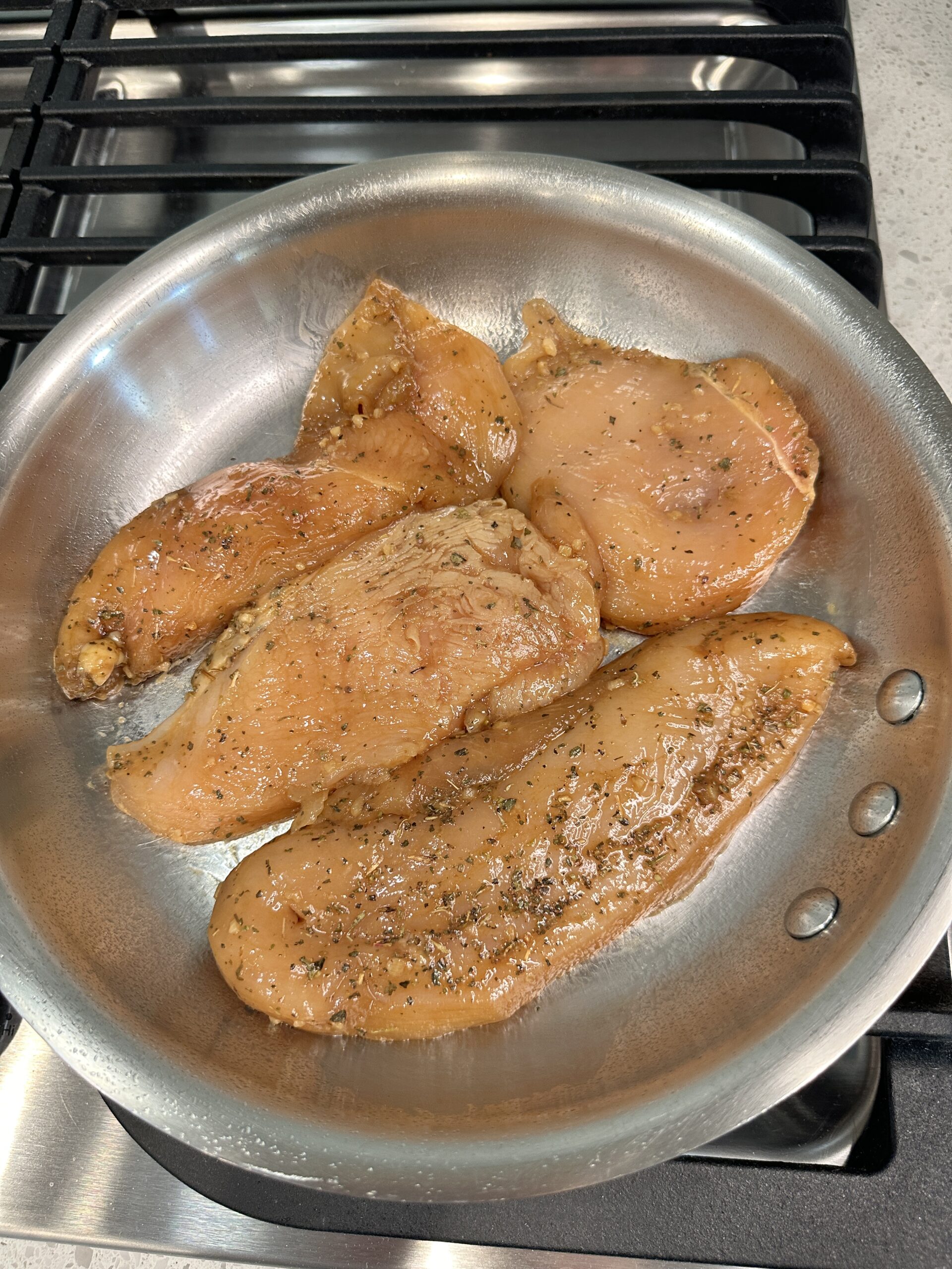 4 marinaded chicken breasts in a skillet.