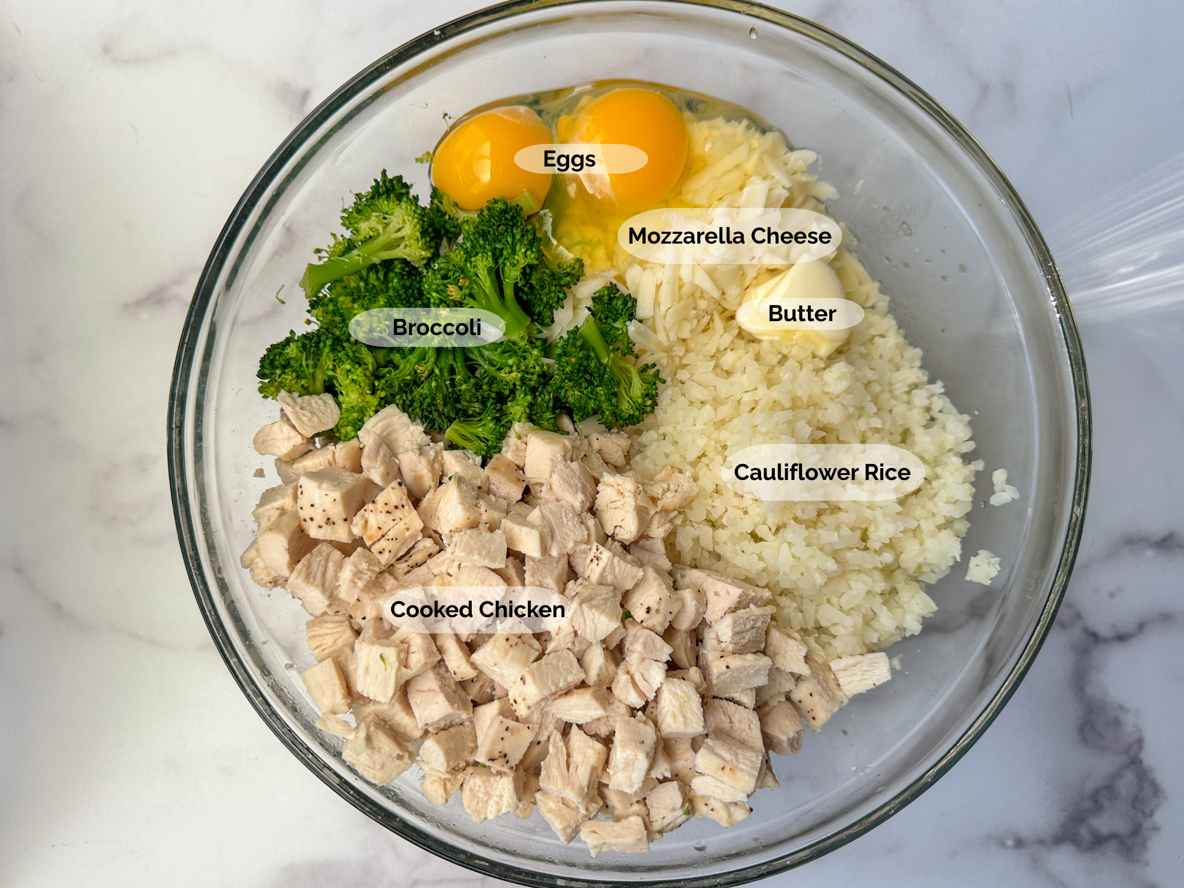 Broccoli Cauliflower Chicken Casserole ingredients: 2 eggs, shredded mozzarella, cauliflower rice, cooked broccoli, and cubed cooked chicken in a large mixing bowl.