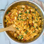 Chicken orzo pasta in a large skillet with cooked spinach