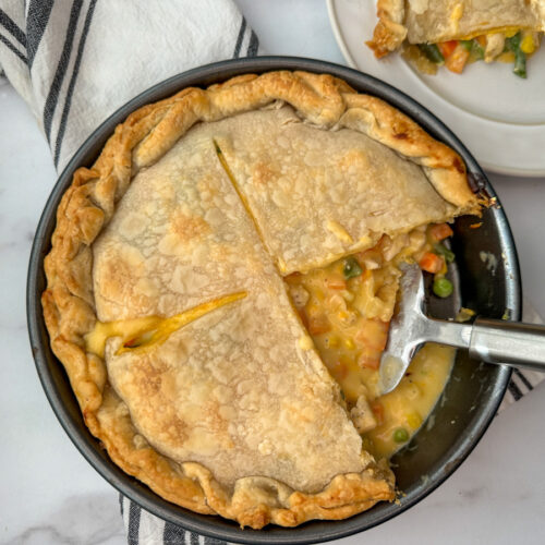 Baked chicken pot pie in a round pie dish with a piece cut out on a plate