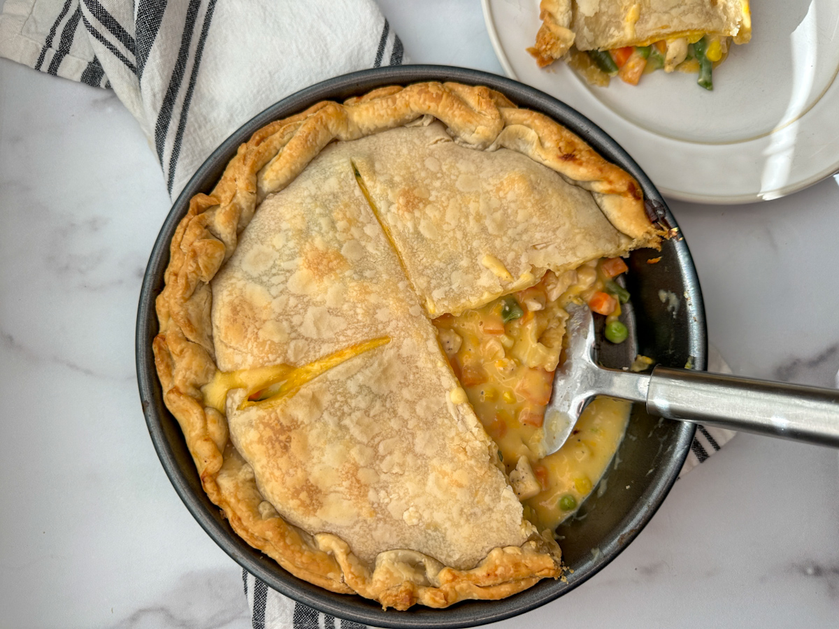 Baked chicken pot pie in a round pie dish with a piece cut out on a plate