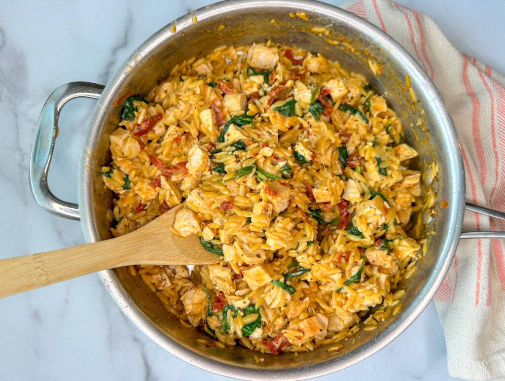 Chicken orzo pasta in a large skillet with cooked spinach