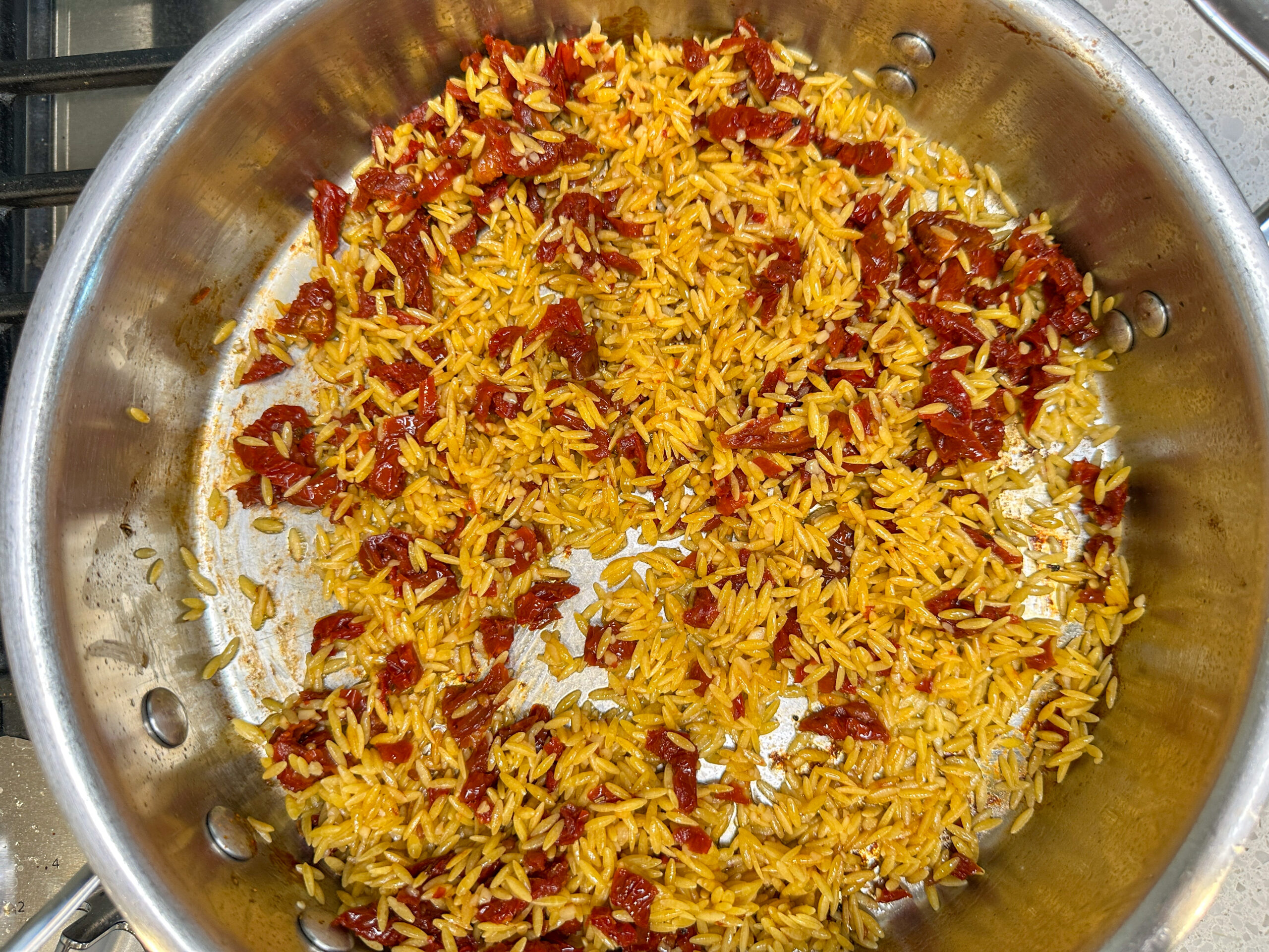 orzo and sun-dried tomatoes cooking in a large skillet.
