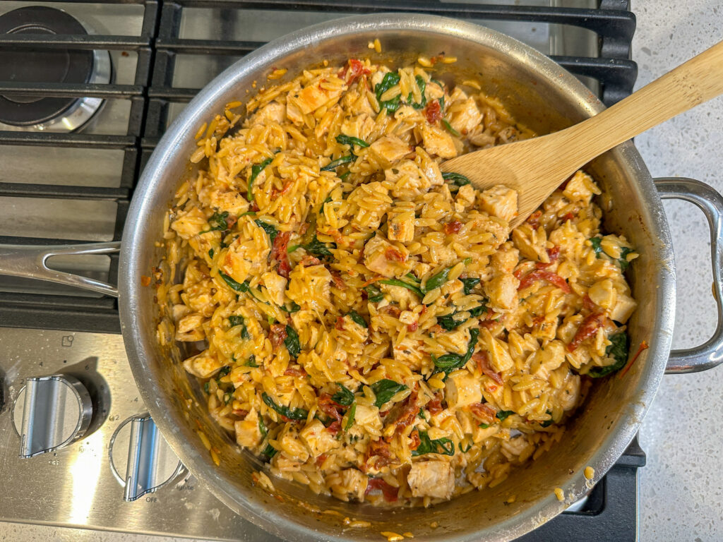cubed chicken, spinach, tomatoes, and creamy orzo in a skillet on a stove top.