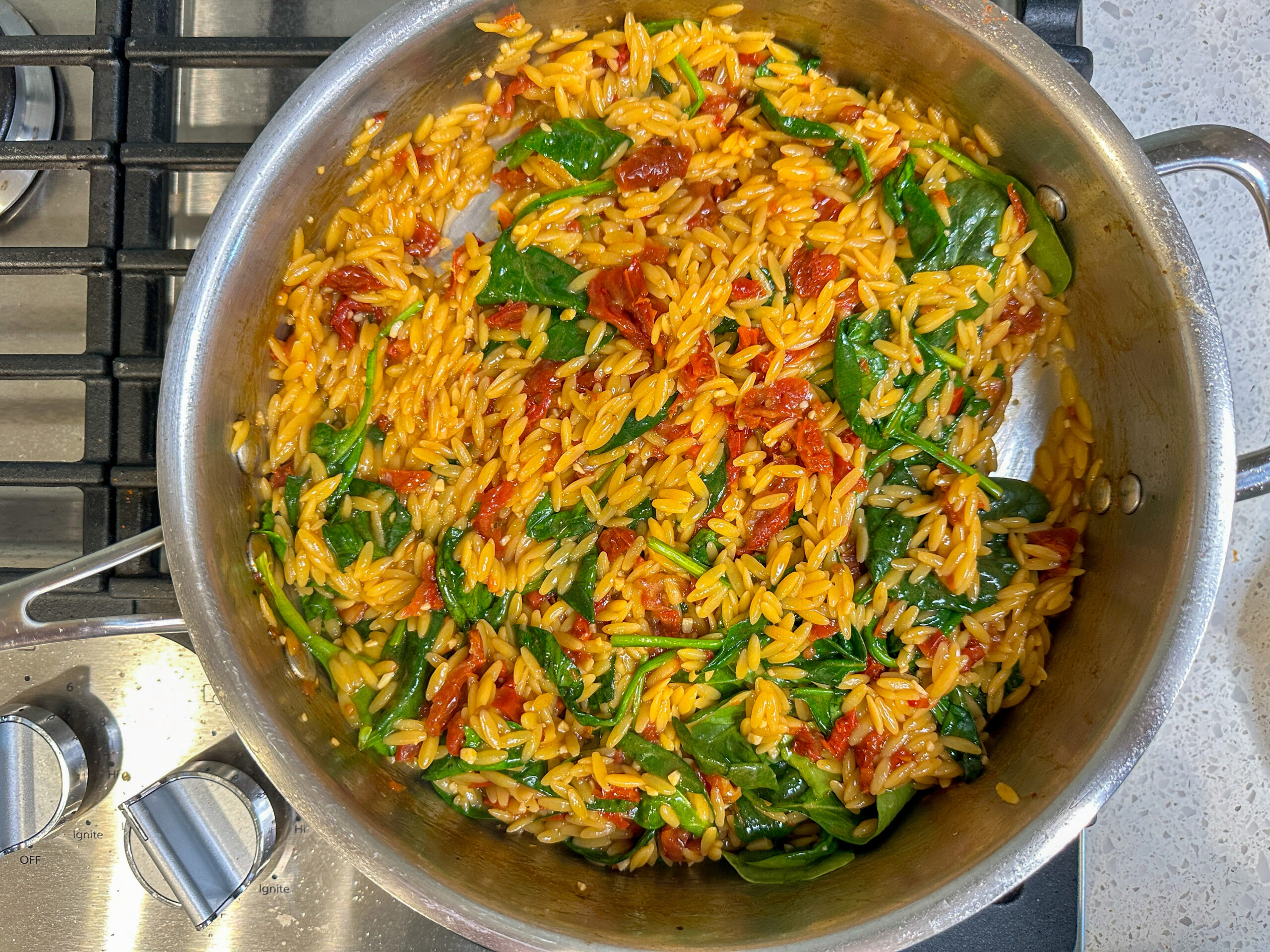 orzo, sun dried tomatoes and spinach cooking in a large skillet.