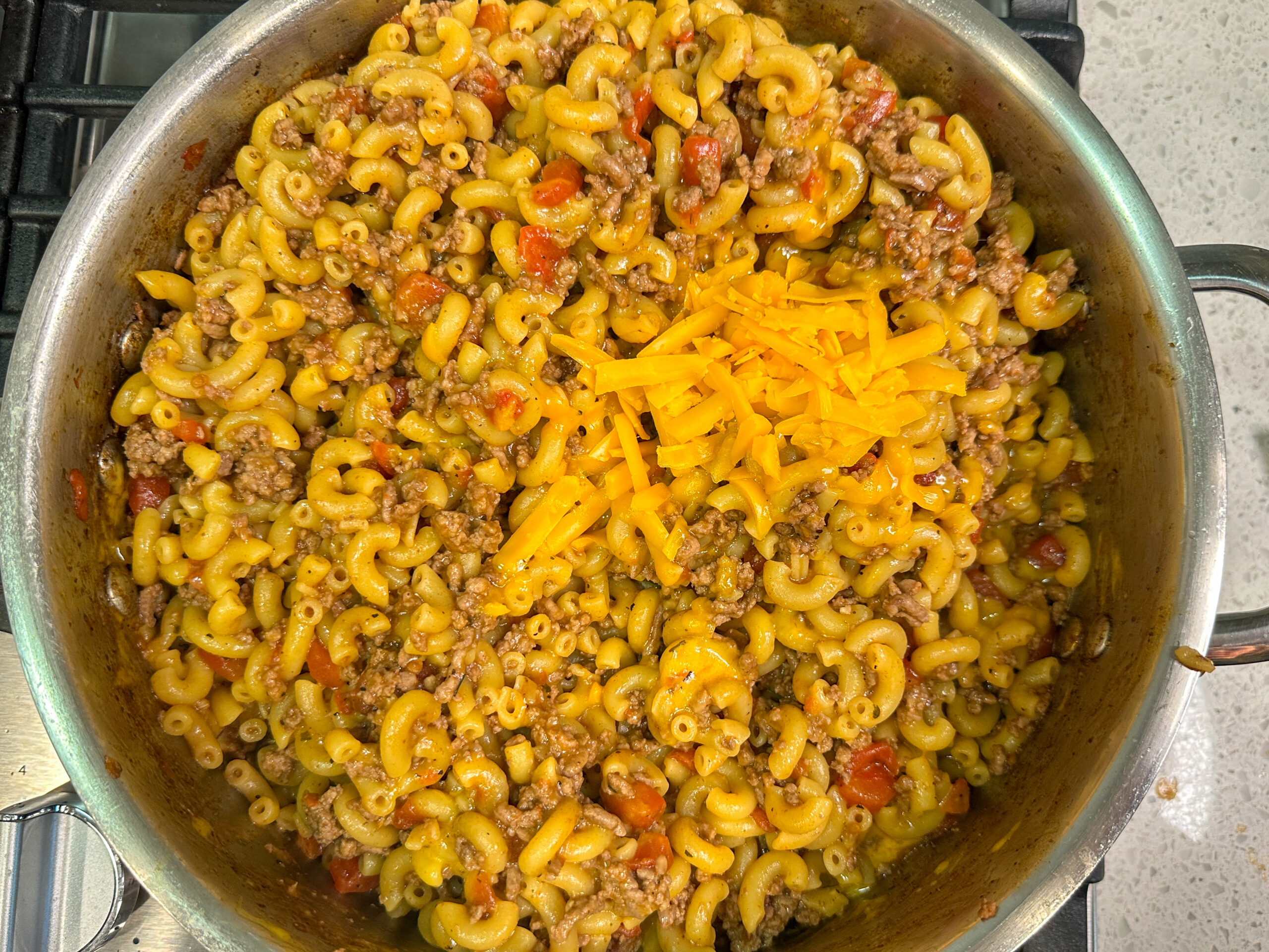 Healthier hamburger helper cooked in a skillet with shredded cheese added on top.