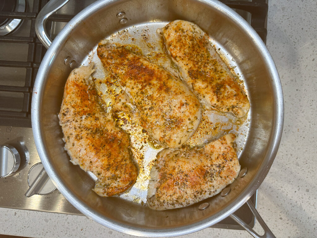 4 chicken breasts seasoned and grilled in a skillet on stove top.