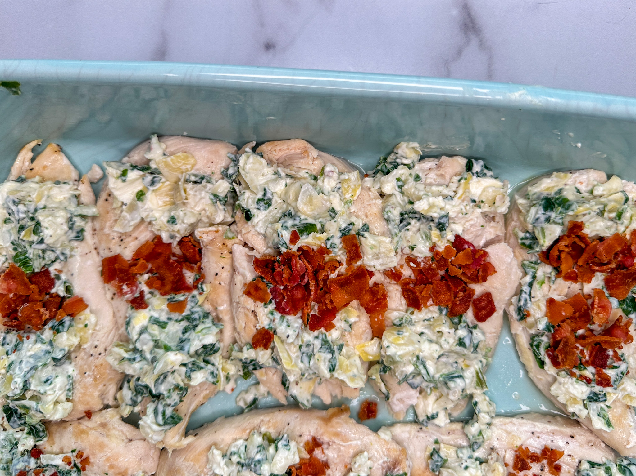 chicken breasts stuffed with cream cheese and spinach mixture with chopped bacon stuffed in alternate slits in a large baking dish.