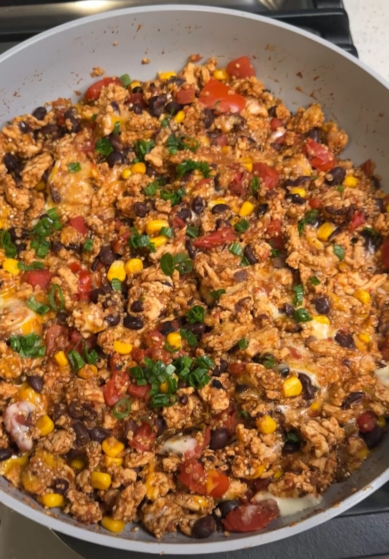cooked turkey taco quinoa in a large skillet with cooked ground turkey, black beans, corn, quinoa, melted cheese, tomatoes, and sliced green onions.