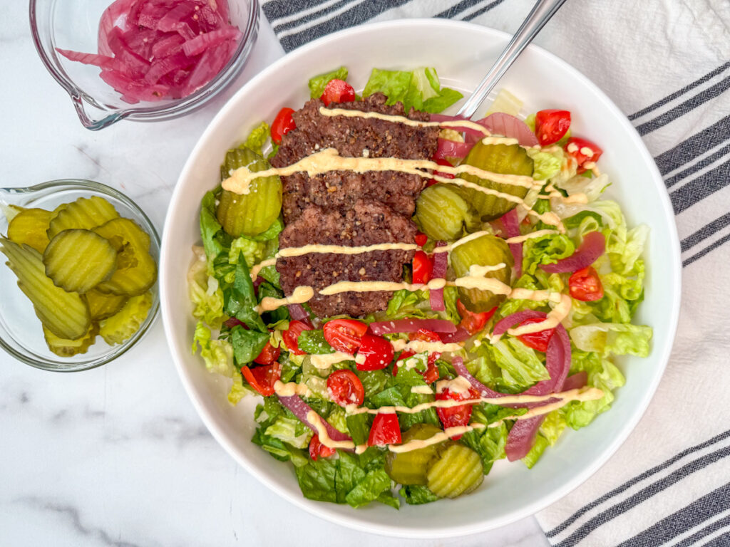 Grilled slider bowl dish in a white bowl with romaine, grilled slider burgers, pickles, tomatoes, and red onion.