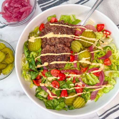 Grilled slider bowl dish in a white bowl with romaine, grilled slider burgers, pickles, tomatoes, and red onion.