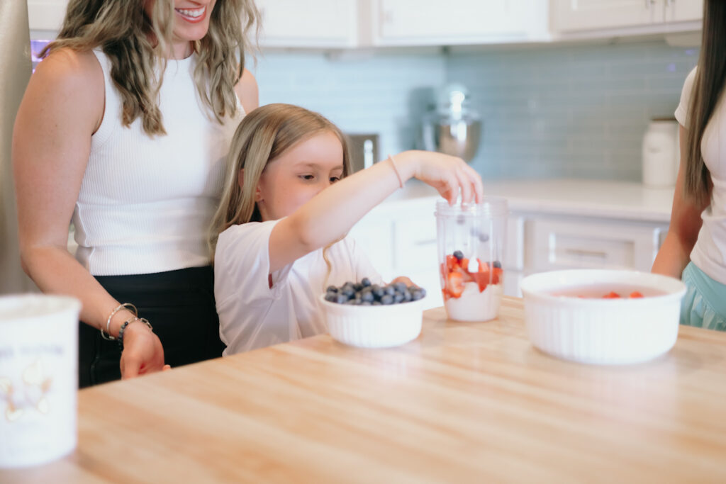 Mom helping kid make lunch smoothie with yogurt and berries
