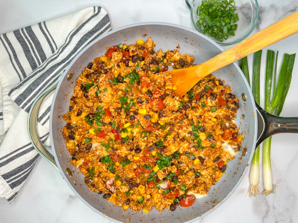 Skillet with cooked ground turkey, black beans, corn, fire roasted tomatoes, melted cheese, and topped with sliced green onions.