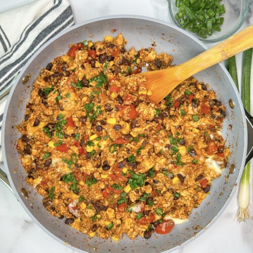 Skillet with cooked ground turkey, black beans, corn, fire roasted tomatoes, melted cheese, and topped with sliced green onions.