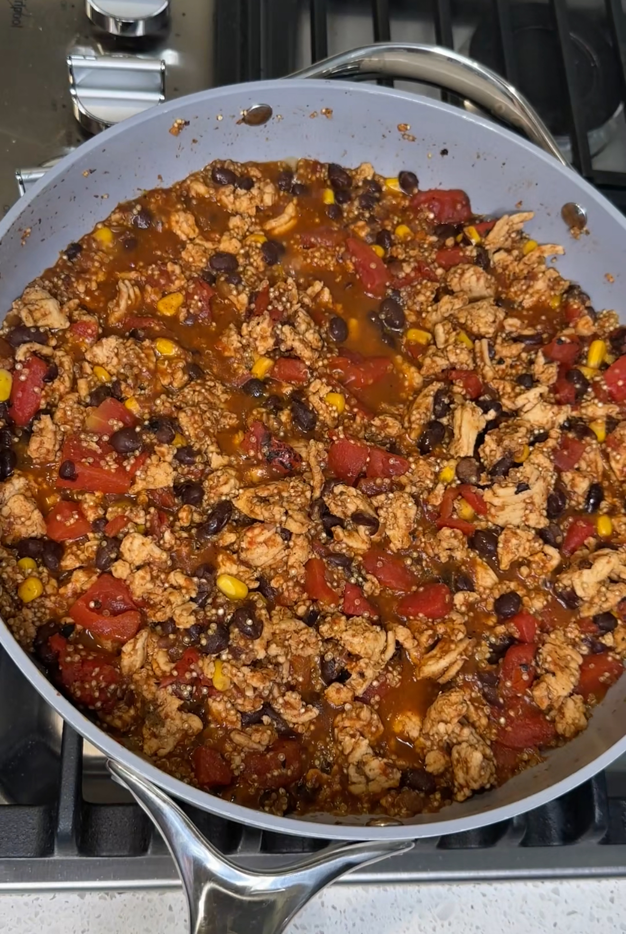 turkey taco quinoa in a large skillet cooking: ground turkey, tomatoes, black beans, corn, and quinoa
