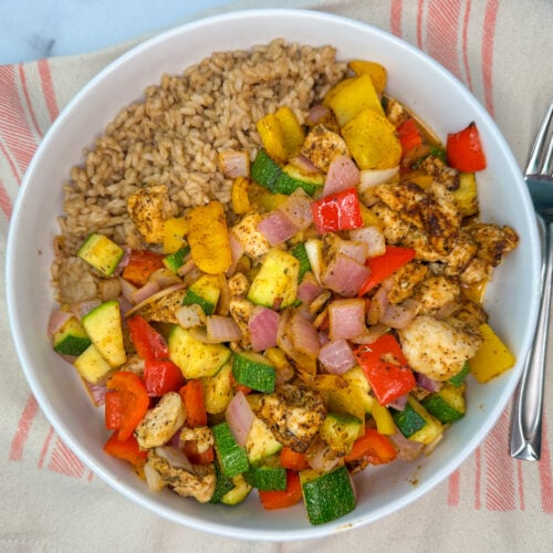 air fryer chicken & veggies with chunks of chicken, diced zucchini, bell peppers, and onion with a side of brown rice in a bowl.