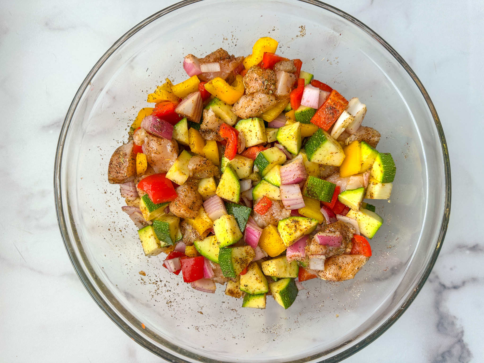 air fryer chicken & veggies ingredients mixed up in a mixing bowl: cubed chicken, chopped zucchini, bell peppers, onion, and seasonings.