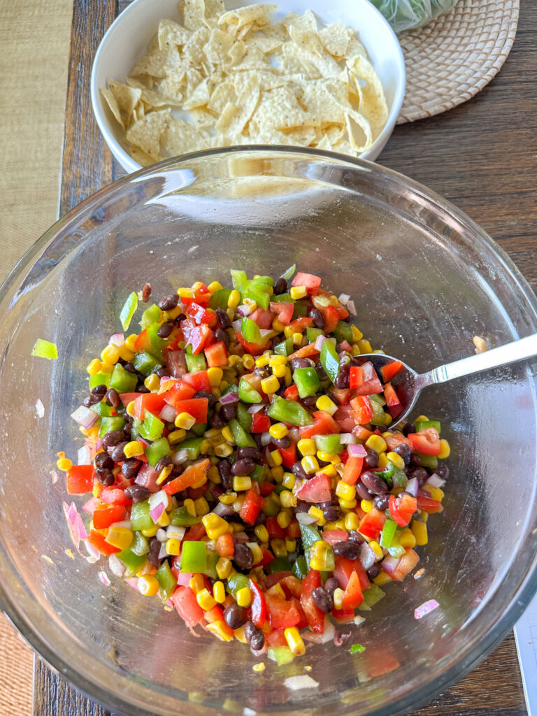 A clear glass bowl full of healthy cowboy caviar ingredients: red and green bell peppers, chopped red onion