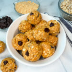 lower calorie protein balls in a white bowl. Several protein balls in the bowl with a few laying off to the side. A side dish of oats and chocolate chips are to the side.
