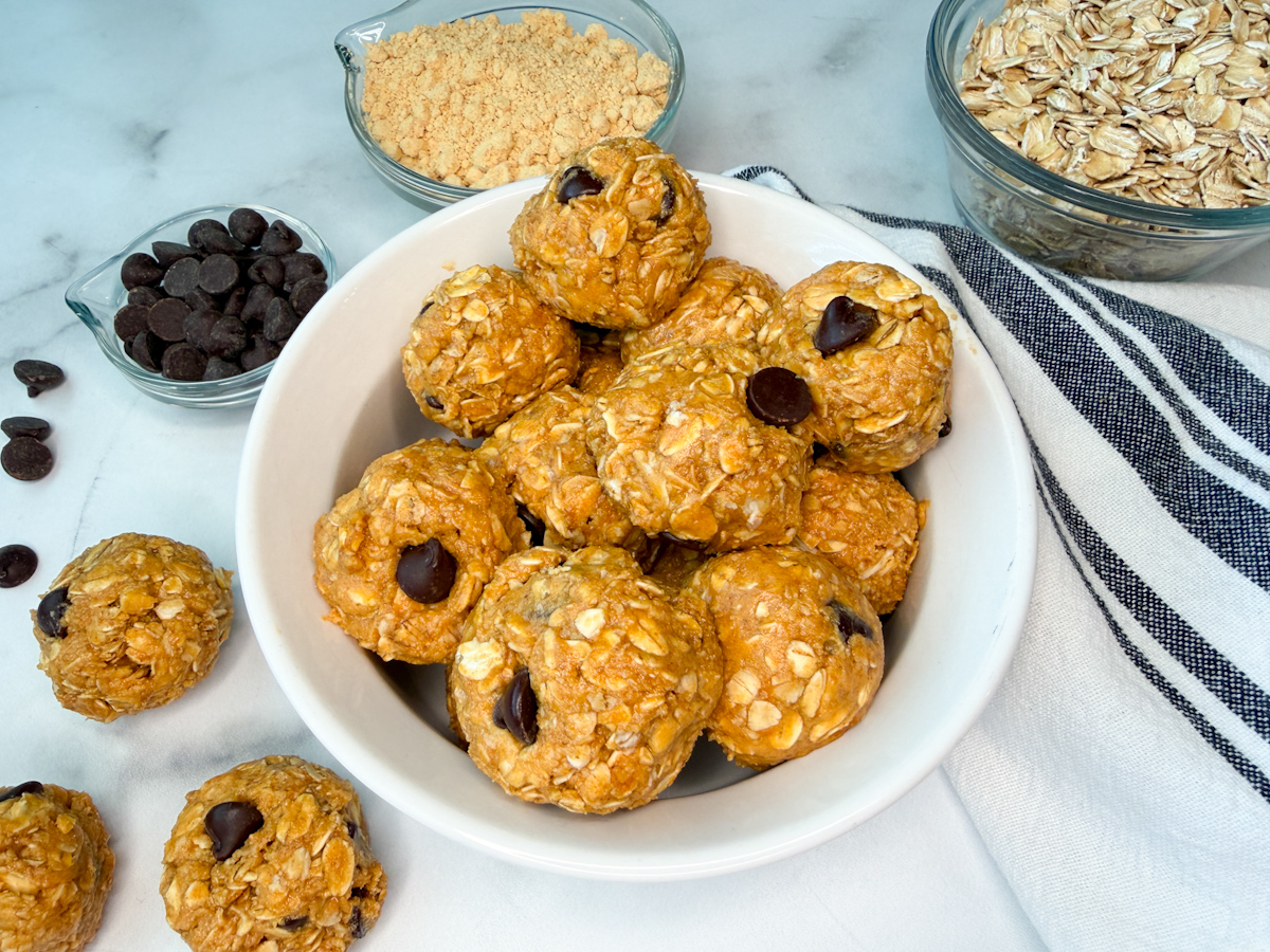 lower calorie protein balls in a white bowl. Several protein balls in the bowl with a few laying off to the side and a side dish of oats and chocolate chips.