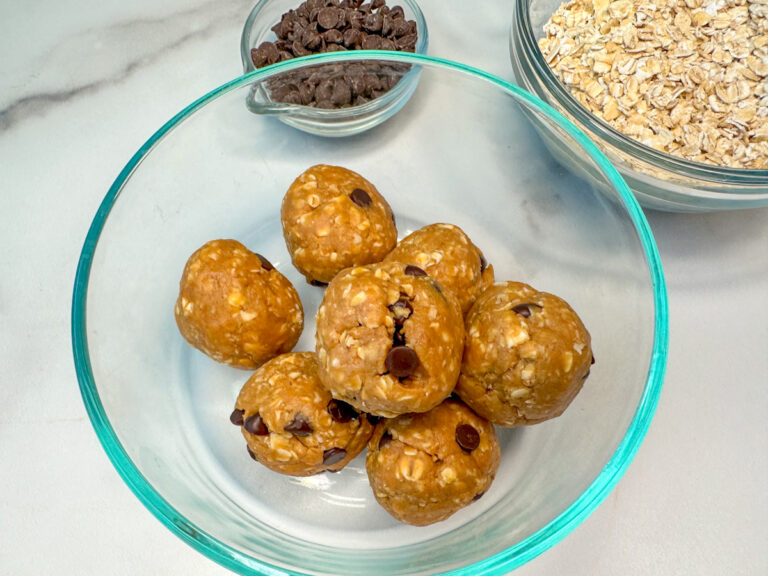 6 rolled protein balls mixed with peanut butter oats, mini chocolate chips, honey, and protein power in a small glass bowl.