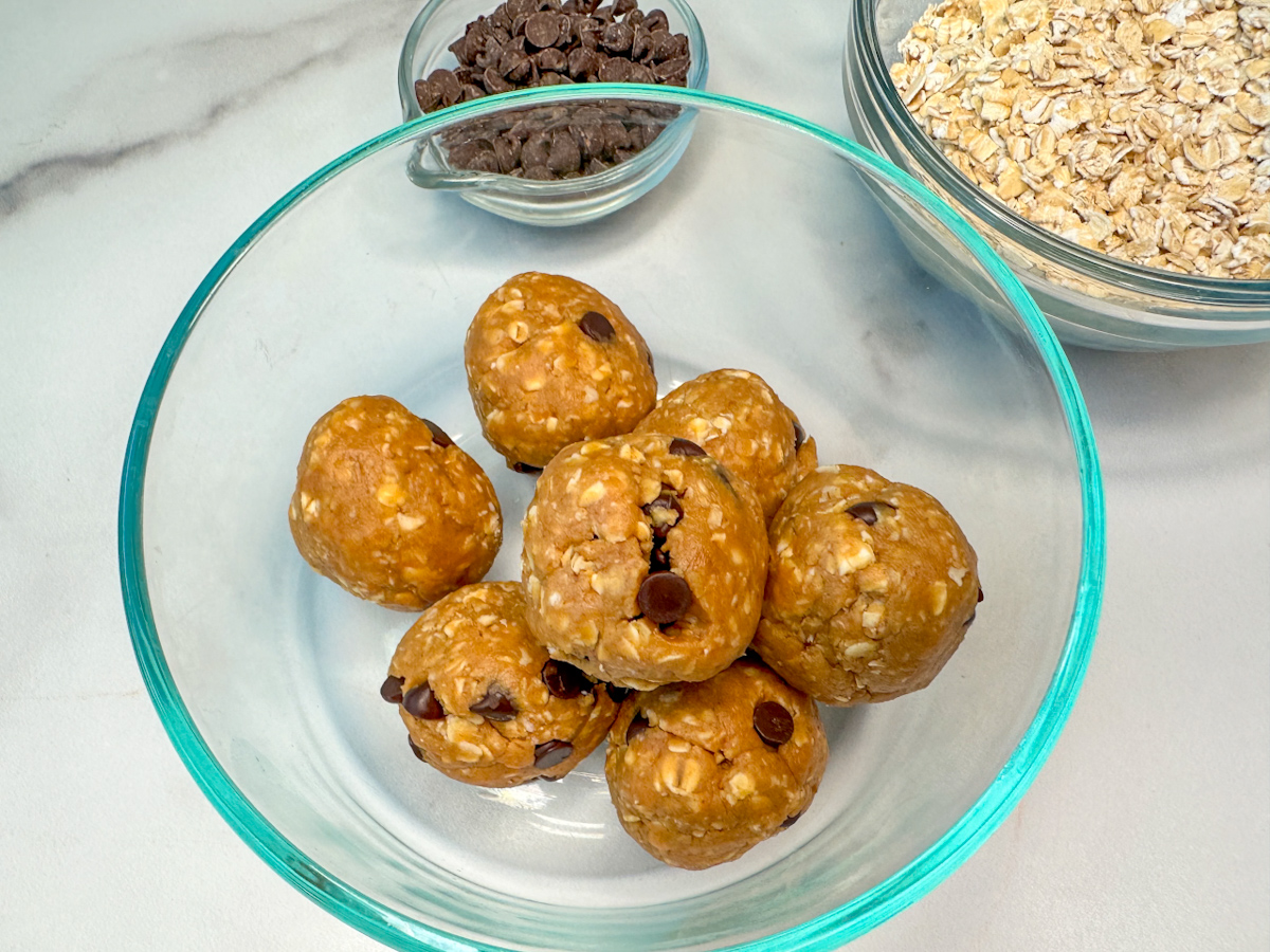 6 rolled protein balls mixed with peanut butter oats, mini chocolate chips, honey, and protein power in a small glass bowl.