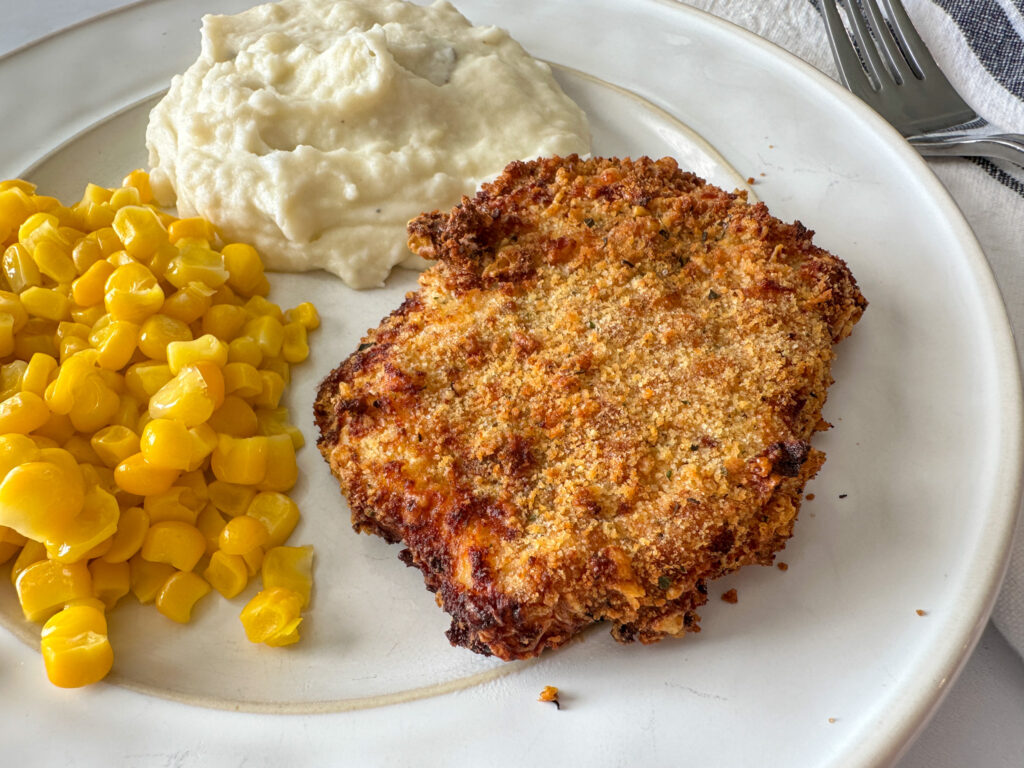 Crispy parmesan pork chops on a plate with mashed potatoes, sweet corn.